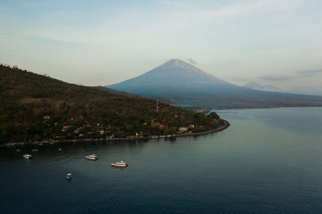 Breathtaking aerial shot of Bali's Mount Agung with tranquil coastal waters at sunrise.